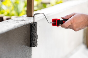 painting a concrete wall with a paint roller and grey paint