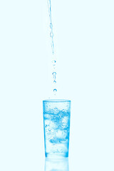 Pouring water into glass with ice isolated on blue background.