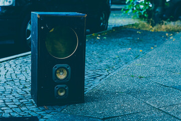 An old scrap loudspeaker standing on the sidewalk, household waste on the sidewalk, broken...