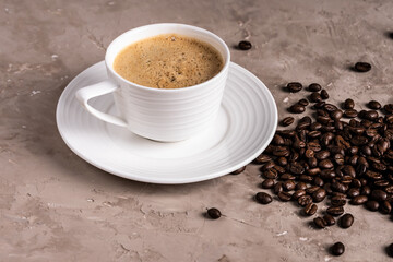 A white cup of coffee, coffee beans are scattered on the table.