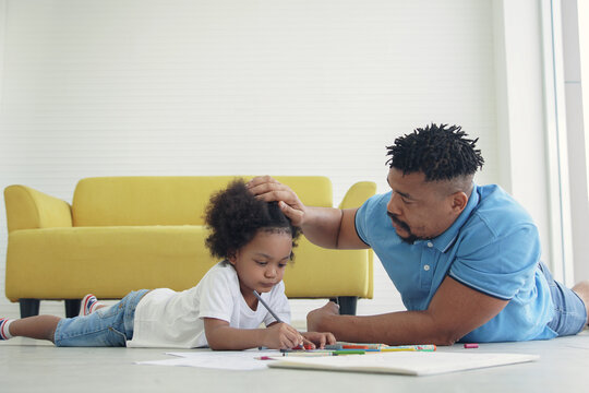 Black African American family dad son drawing together at home. Young father lying on the floor and take care his kid child boy while drawing coloring pictures
