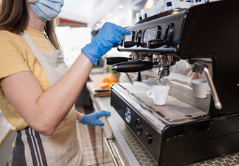 Caucasian woman working in a bar presses the button on the coffee machine she wears protective face mask and gloves - Following the safety measures - Concept of the new normality
