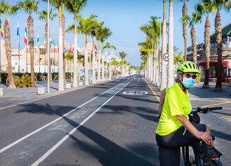 Alone woman with yellow helmet and tshirt cycling in Tenerife in the deserted city street due to coronavirus, tourism crisis - new normal for a retired people