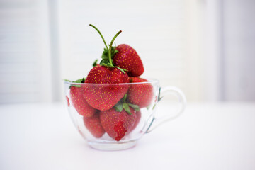 Red strawberries in a transparent dish on a white table, in the interior