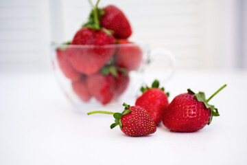 Red strawberries in a transparent dish on a white table, in the interior