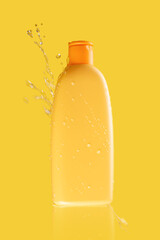 Yellow bottle of cosmetics on a yellow background in water splashes and drops, water splash, splashes