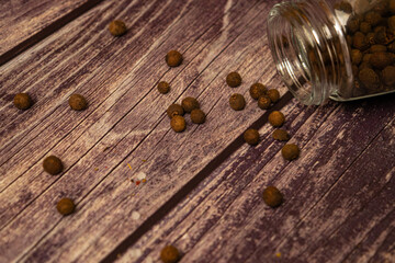 Black allspice scattered on a wooden background and a glass spice jar with black pepper lying on its side. Close up.