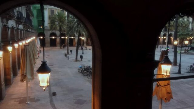 The Royal square of Barcelona at dusk with lights on. A few people walking by during the COVID-19 social distancing.