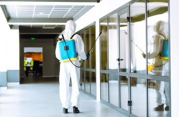 Contractor disinfecting office for COVID-19 coronavirus. A disinfector man in a protective suit and...