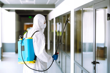 Contractor disinfecting office for COVID-19 coronavirus. A disinfector man in a protective suit and...