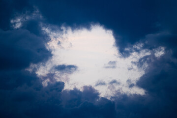 Sky frame surrounded by dark blue storm clouds at sunset. Stock photo of a round natural patch of sky surrounded by clouds.