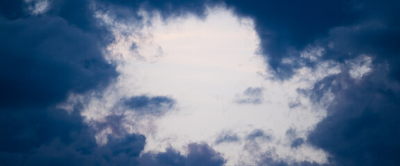 Sky surrounded by dark blue storm clouds at sunset. Stock panoramic photo of natural frames by clouds.