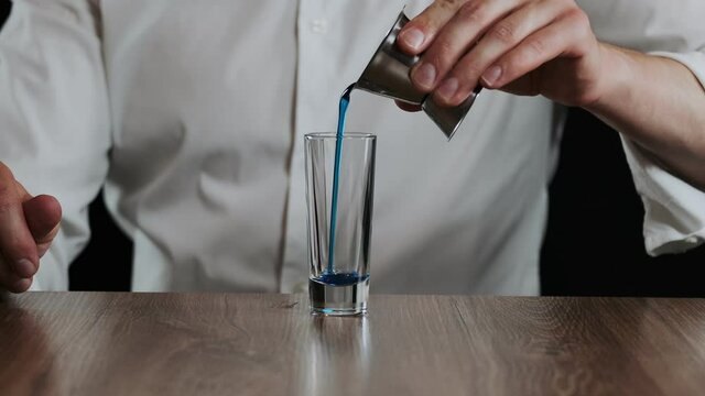 Bartender pouring blue curacao liquor into glass from jigger. Close up