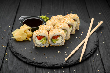 Sushi rolls in sesame with avocado, salmon and cream cheese on a black background