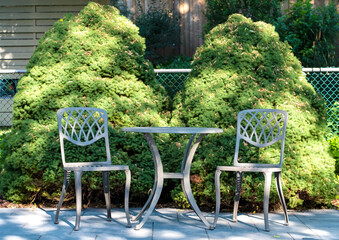 A Bistro Set on a Stone Patio in Front of Two Dwarf Pine Trees in an Idyllic Garden