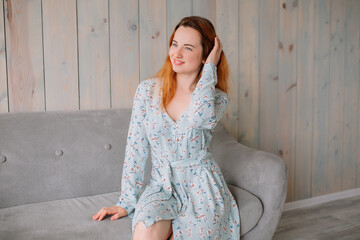 Fototapeta premium Beautiful girl with red hair in a blue print dress with flowers smiles in the photo