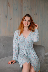 Fototapeta premium Beautiful girl with red hair in a blue print dress with flowers smiles in the photo