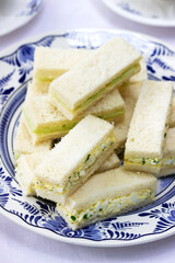 Afternoon tea in the garden, finger sandwiches with cucumber and egg salad and tea on a light background.