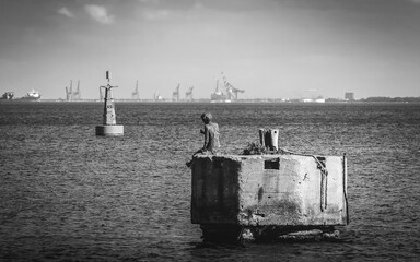 Denkmal Statue neben einer Boje im Wasser am Hafen von Gdynia in der Danziger Bucht. Wahrzeichen an der Küste der Ostsee als trauriges Mahnmal in dunklem, düsteren monochrom schwarzweiss.