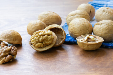 Whole walnuts and walnut kernel halves without shell on a dark wooden table and checkered towel, close up. Seeds of the common walnut tree Juglans regia. Macro food photo close up view.