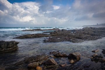 Ocean landscape with rocks in the foreground and big clouds forming in the background. 
