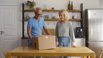 Happy senior couple open cardboard delivery box in kitchen - Powered by Adobe