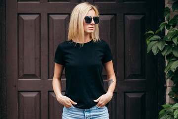 Stylish blonde girl wearing black t-shirt and glasses posing against street , urban clothing style....