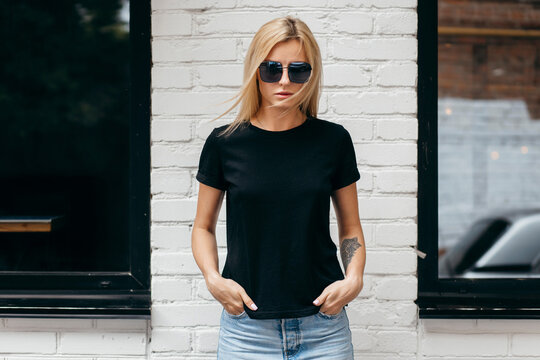 Stylish blonde girl wearing black t-shirt and glasses posing against street , urban clothing style. Street photography
