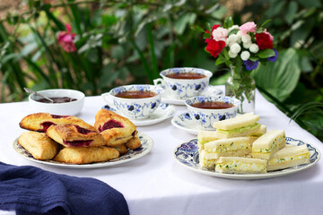 Afternoon tea in the garden with scones, strawberry jam, finger sandwiches with cucumber and egg...