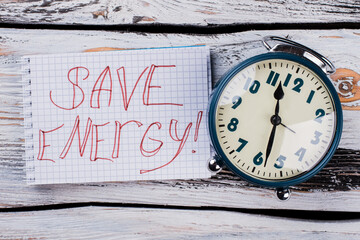 Save enegry tagline and alarm clock. White wooden table surface on the background.