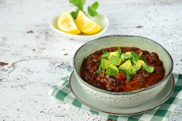 Homemade vegan black bean chili tomato soup with diced avocado and chopped parsley served with lemon