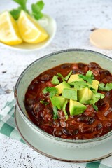 Homemade vegan black bean chili tomato soup with diced avocado and chopped parsley served with lemon