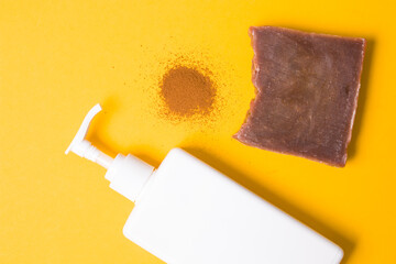 white bottle with dispenser without a label, a heap of ground coffee, a piece of natural homemade brown cocoa soap on a yellow background, natural body care at home