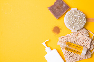 white bottle with dispenser without a label, a dry massage brush, body oil, a pile of ground coffee, a knitted cotton washcloth, natural cocoa soap on a yellow background, natural body care