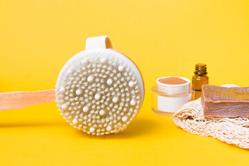 dry anti-cellulite massage brush, jar of ground coffee, knitted cotton washcloth, natural cocoa soap on a yellow background