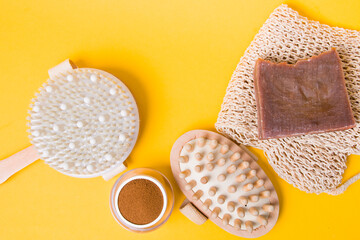 jar of ground coffee, brush for dry anti-cellulite massage, a knitted washcloth, homemade cocoa soap, a wooden massager on a yellow background, close-up, home body care, zero waste lifestyle