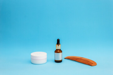 white round cream jar, pipette jar, wooden comb are on a blue sky background, front view