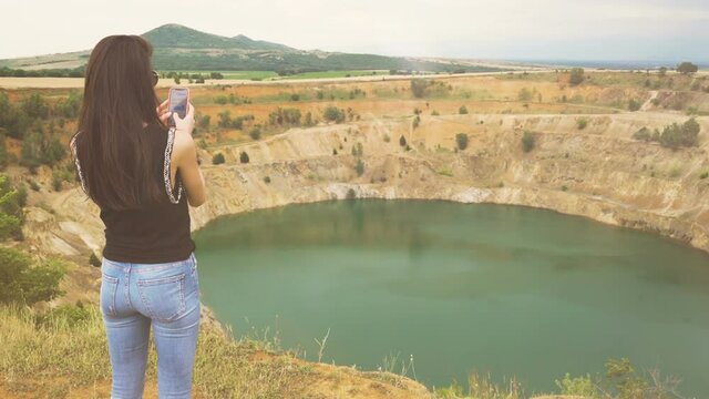 Back view of young woman using her smartphone to take photos of copper open mine pit in Bulgaria