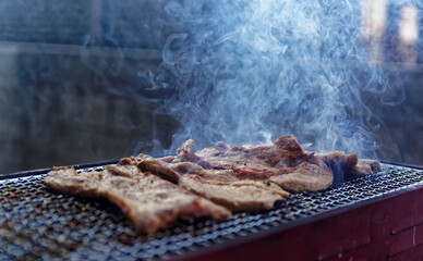 Strips of meat smoking and steaming on a grill
