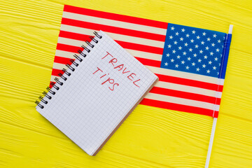 USA travel tips concept. Close up US flag and notepad on yellow wooden table.