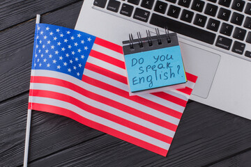 Do you speak english. American flag and laptop pc on dark wooden table. Top view flat lay.