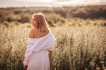 Young busty girl in a white dress on an oat field.