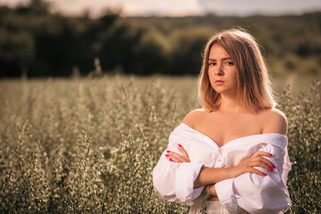 Fototapeta na wymiar Young busty girl in a white dress on an oat field.