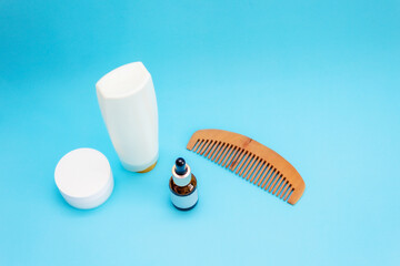 Obraz premium white round cream jar, pipette jar, wooden comb, large white bottle are on a blue sky background, front view