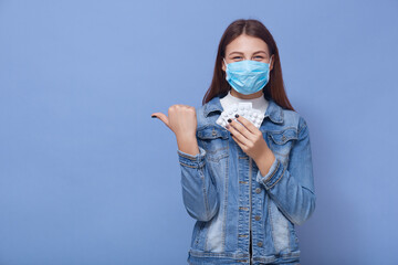 Smiling woman posing isolated over blue background. Female wearing medical sterile face mask...