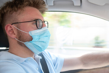Young business man driving with a Covid-19 protective face mask on.