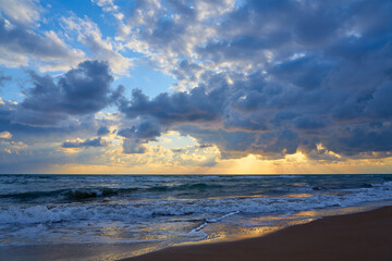 Sandy beach on a sunset with reflection on wet sand and waves with foam. Copy space.