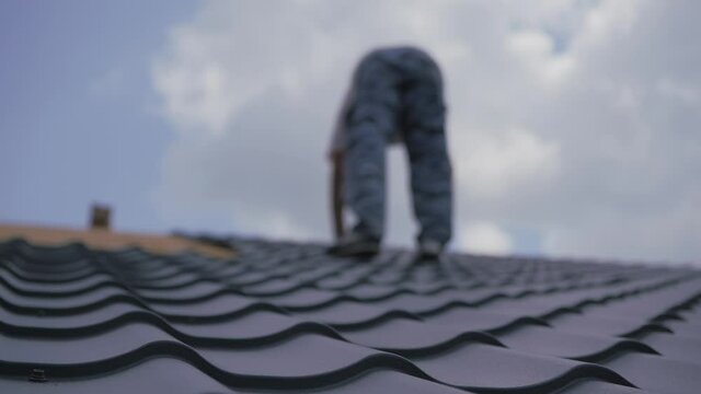 Roofing works. The installer screws the metal tile to the roof crate. Roof construction.
