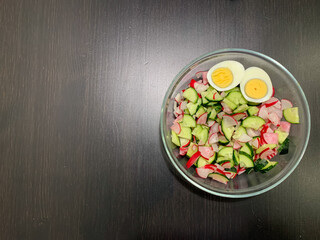 In the photo, a salad of chicken egg, radish, cucumber on a dark wooden table. Photo from above. Proper nutrition, vegetarian diet.