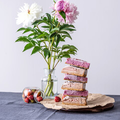 Brown and pink pieces of mousse raw cake are arranged in the form of a pyramid one on top of the other. Next to it is a vase of flowers and berries. Concept of healthy and delicious trendy desserts